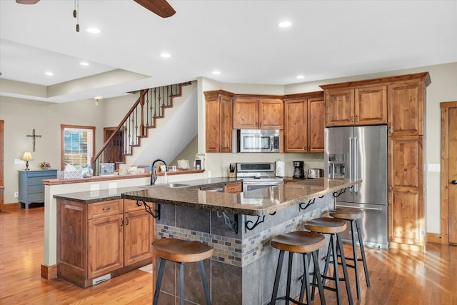 kitchen with stainless steel appliances, dark stone counters, a peninsula, and a kitchen breakfast bar