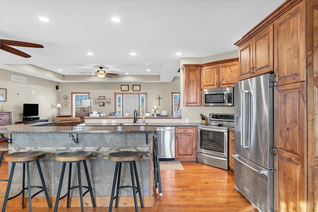 kitchen featuring visible vents, open floor plan, stainless steel appliances, light wood-style floors, and a kitchen bar