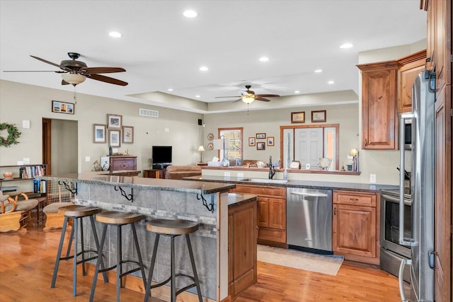 kitchen with a sink, stainless steel appliances, brown cabinetry, and a kitchen bar