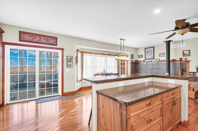 kitchen with a peninsula, light wood-style floors, dark stone countertops, a kitchen bar, and decorative light fixtures