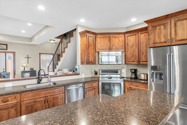 kitchen featuring dark stone counters, appliances with stainless steel finishes, brown cabinetry, and a sink