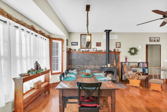 dining area featuring a wood stove, light wood-style flooring, visible vents, and a ceiling fan