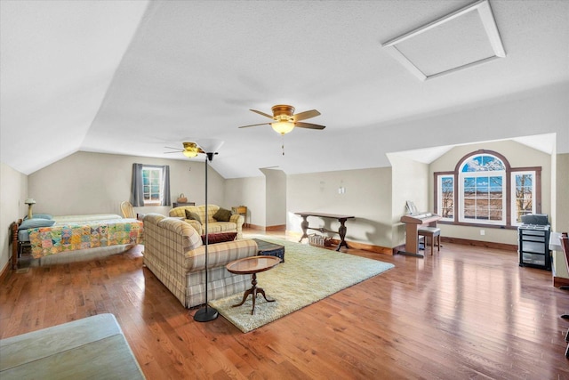 living area featuring attic access, vaulted ceiling, baseboards, and wood-type flooring