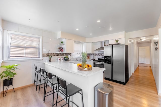 kitchen with appliances with stainless steel finishes, white cabinets, decorative backsplash, kitchen peninsula, and wall chimney exhaust hood