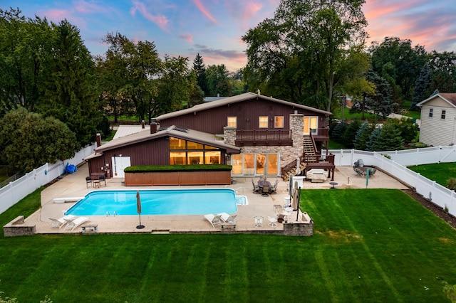 back house at dusk featuring a balcony, a fenced in pool, a patio, and a lawn