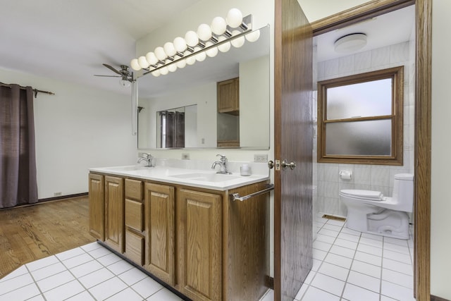 bathroom with toilet, tile walls, vanity, ceiling fan, and tile patterned flooring