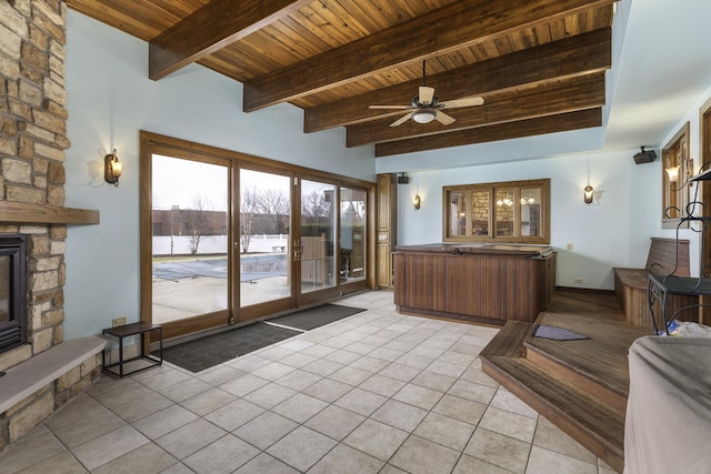 tiled living room with beam ceiling, ceiling fan, a stone fireplace, and wood ceiling