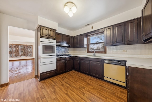 kitchen featuring dark brown cabinetry, sink, light wood-type flooring, dishwashing machine, and oven