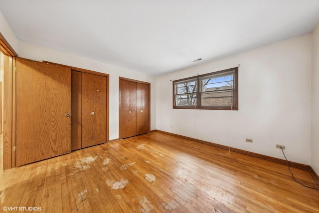 unfurnished bedroom featuring multiple closets and light hardwood / wood-style flooring