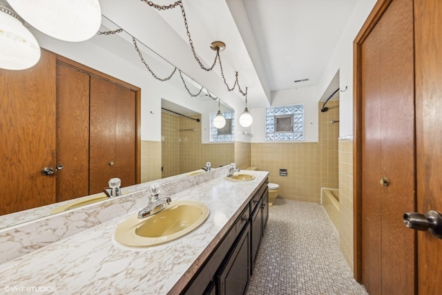 full bathroom with tile walls, tiled shower / bath combo, vanity, toilet, and tile patterned floors