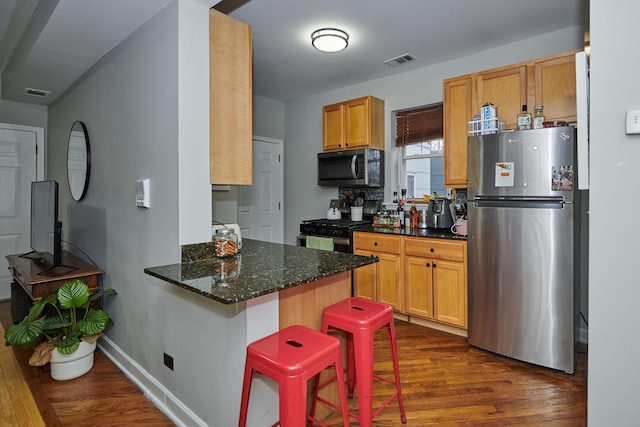 kitchen with stainless steel refrigerator, a kitchen bar, dark stone counters, kitchen peninsula, and dark wood-type flooring