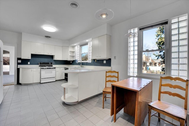 kitchen featuring decorative light fixtures, sink, white cabinets, backsplash, and white range oven