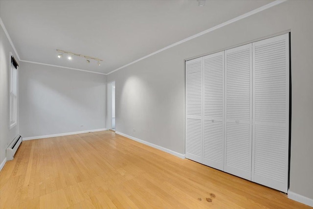 unfurnished bedroom featuring a baseboard heating unit, track lighting, ornamental molding, and a closet