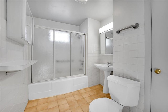 bathroom with toilet, bath / shower combo with glass door, tile patterned flooring, and tile walls