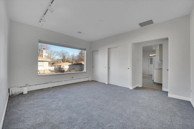 unfurnished bedroom featuring a baseboard heating unit, two closets, track lighting, and carpet flooring