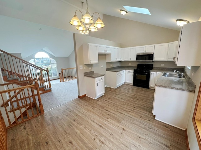 kitchen featuring black gas range oven, sink, white cabinetry, hanging light fixtures, and a skylight