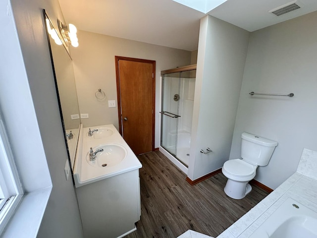 bathroom featuring a skylight, wood-type flooring, vanity, walk in shower, and toilet