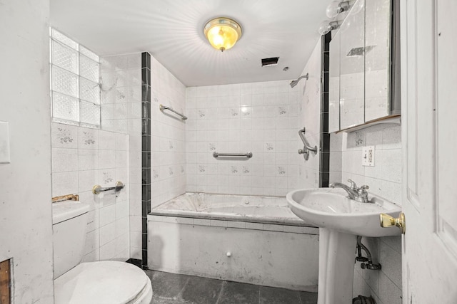 bathroom featuring toilet, tiled shower / bath combo, and tile walls