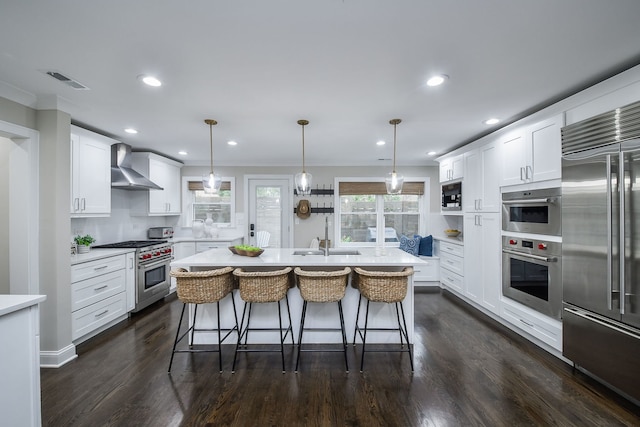 kitchen featuring pendant lighting, wall chimney exhaust hood, built in appliances, and white cabinets