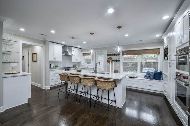 kitchen featuring pendant lighting, an island with sink, wall chimney exhaust hood, and white cabinets