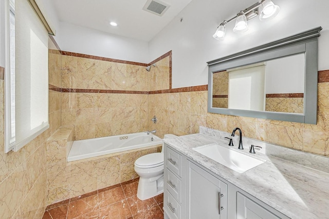 full bathroom with tiled shower / bath, vanity, toilet, and tile walls