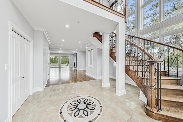 foyer entrance with ornamental molding, decorative columns, and a high ceiling