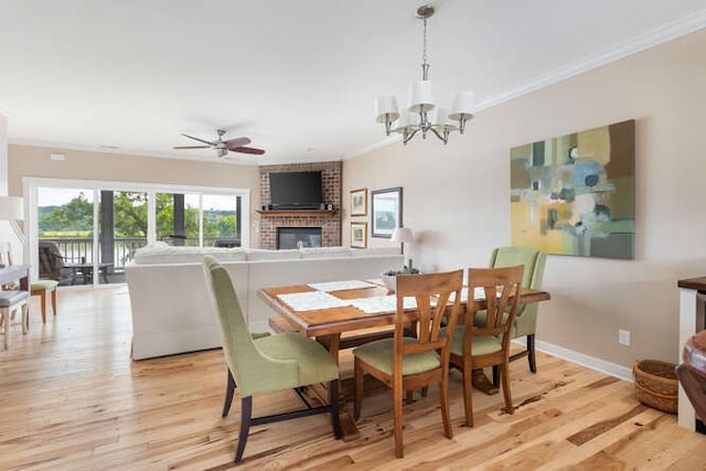 dining area with ornamental molding, ceiling fan with notable chandelier, a fireplace, and light wood-type flooring