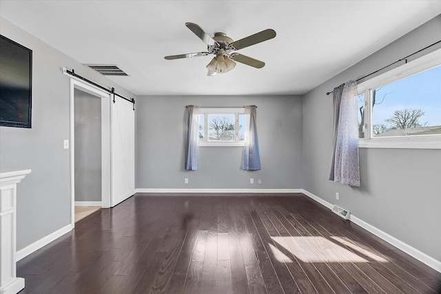 unfurnished bedroom featuring ceiling fan, a barn door, and dark hardwood / wood-style flooring