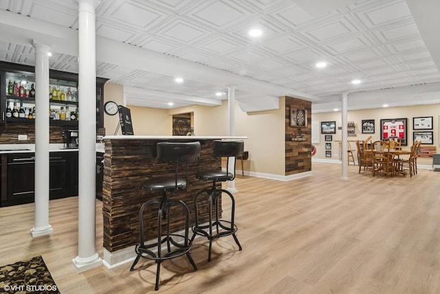 bar featuring decorative columns, baseboards, indoor bar, an ornate ceiling, and light wood-type flooring