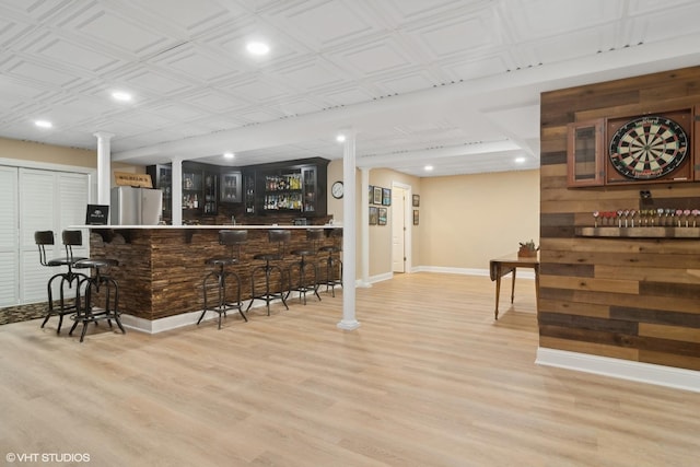 bar with freestanding refrigerator, light wood-style flooring, and a bar