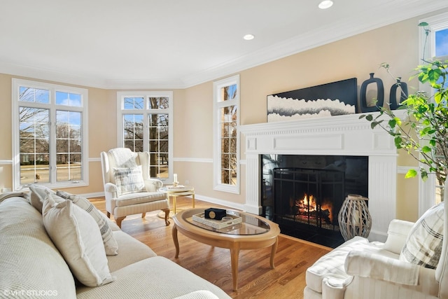 living room with recessed lighting, wood finished floors, a fireplace with flush hearth, baseboards, and crown molding