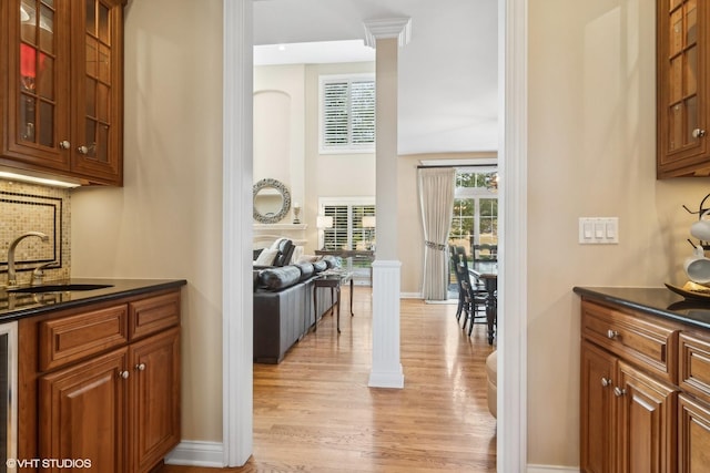 kitchen featuring a sink, light wood-type flooring, decorative backsplash, brown cabinetry, and glass insert cabinets