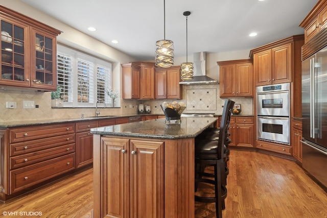 kitchen featuring brown cabinets, wall chimney exhaust hood, stainless steel appliances, and a center island