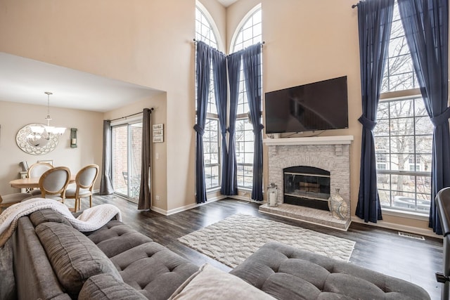 living room with a stone fireplace, plenty of natural light, dark hardwood / wood-style floors, and a towering ceiling