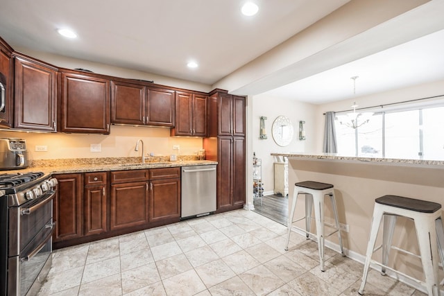 kitchen featuring sink, a breakfast bar area, appliances with stainless steel finishes, light stone counters, and a chandelier