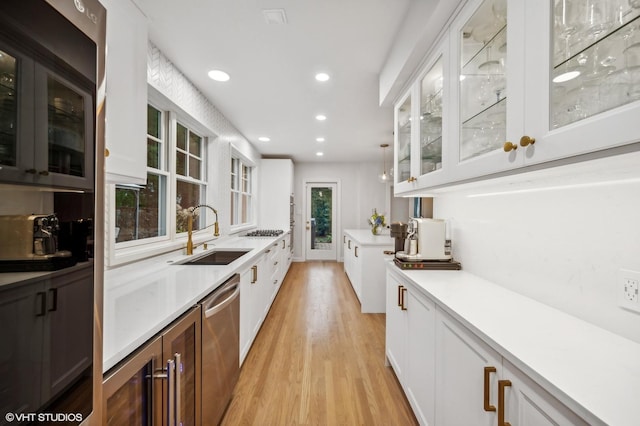 bar featuring dishwasher, sink, light hardwood / wood-style flooring, and white cabinets