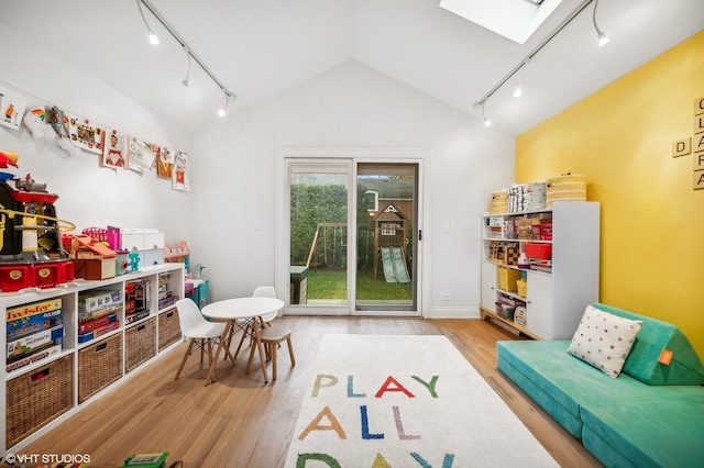 game room with track lighting, vaulted ceiling with skylight, and light hardwood / wood-style flooring