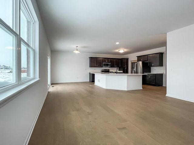 kitchen with dark brown cabinetry, stainless steel appliances, a kitchen island with sink, and wood-type flooring