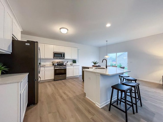 kitchen with pendant lighting, white cabinets, a kitchen island with sink, stainless steel appliances, and light hardwood / wood-style flooring