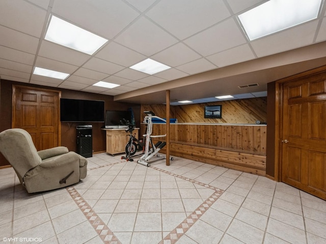 interior space featuring a paneled ceiling, wooden walls, and light tile patterned floors