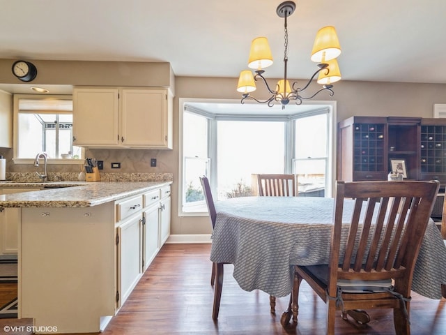 kitchen with hanging light fixtures, hardwood / wood-style floors, white cabinets, and light stone counters