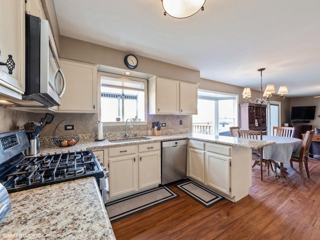 kitchen with appliances with stainless steel finishes, sink, dark wood-type flooring, and decorative light fixtures