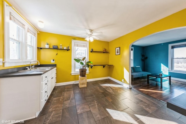 kitchen with arched walkways, dark countertops, white cabinetry, a sink, and baseboards