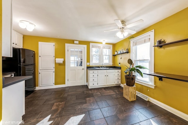 kitchen with stone tile floors, white cabinetry, baseboards, freestanding refrigerator, and dark countertops