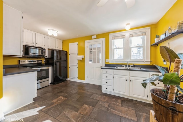 kitchen featuring stainless steel appliances, dark countertops, stone finish floor, white cabinets, and a sink