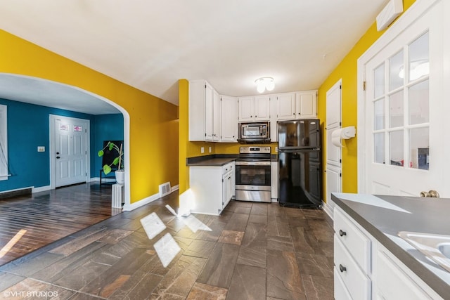 kitchen with arched walkways, baseboards, dark countertops, appliances with stainless steel finishes, and white cabinetry