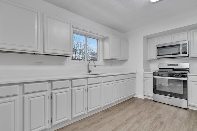 kitchen with appliances with stainless steel finishes, sink, white cabinets, and light hardwood / wood-style floors