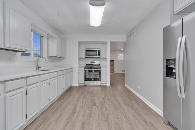 kitchen featuring sink, appliances with stainless steel finishes, light hardwood / wood-style floors, a textured ceiling, and white cabinets