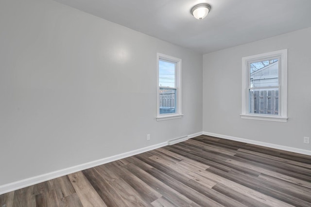 unfurnished room with dark wood-type flooring, a baseboard radiator, and a wealth of natural light