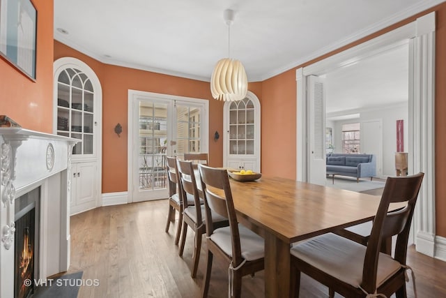 dining area with a warm lit fireplace, wood finished floors, baseboards, french doors, and crown molding